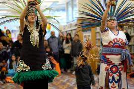 Два исполнителя в головных уборах с большими перьями ведут культурное празднование Día de los Ninos в библиотеке Gresham.
