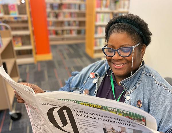 Black staff member smiling and reading open newspaper