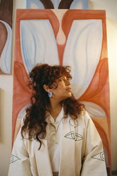 Artist Salomée Souag looks to the side while posed in front of a painting with white and reddish shape.