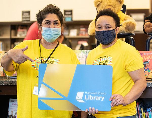 Two library staff holding a giant library card