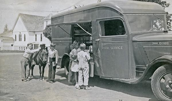 Young patrons crowd outside a library bus many decades ago