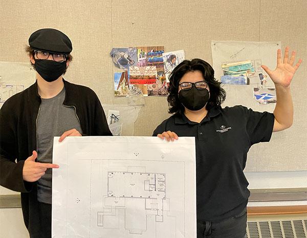Two teens hold up a design plan for a library