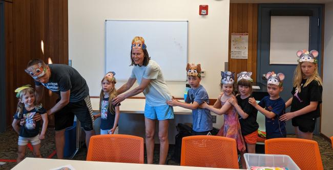 Children and parents from the book club playing a game and wearing hats. 