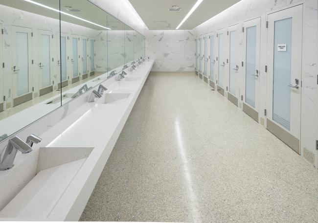 Inside the gender inclusive bathrooms, it is a long room with doors to restrooms on the right and many sinks for handwashing to the left