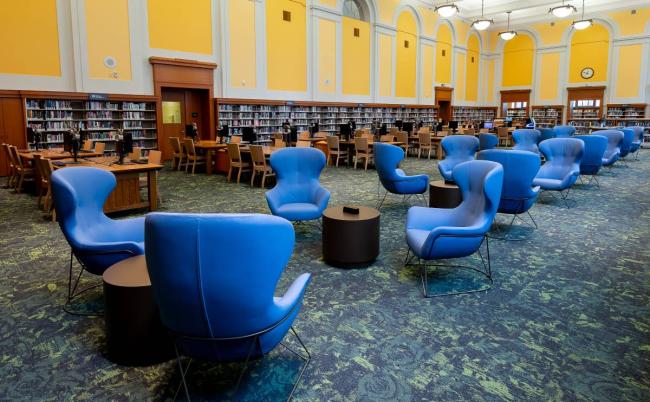 Alt text for image: Soft blue seats are centered in a yellow room with bookshelves lining the walls