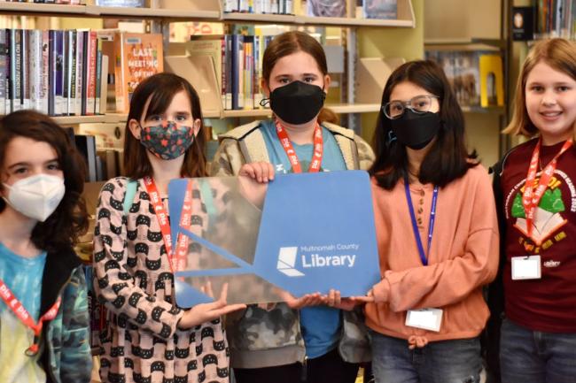 Five tweens inside the library holding a big library card